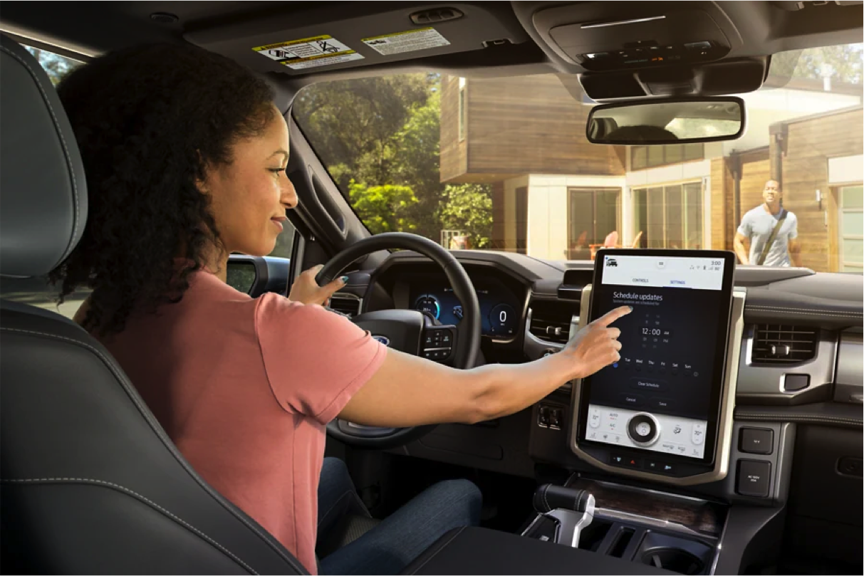 A woman sits in a car, and scheduling updates on a large touchscreen of a Car.