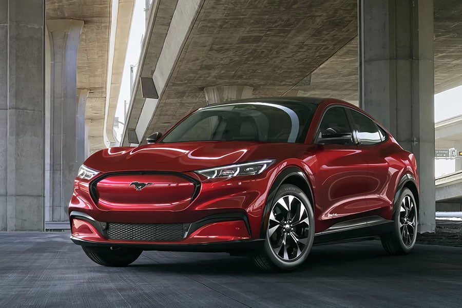A red Ford Mustang Mach-E electric SUV parked under an overpass with concrete pillars.