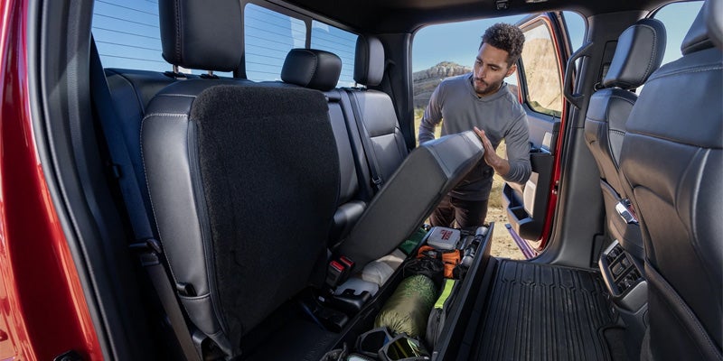 Man lifting a passenger seat in a truck to reveal built-in under-seat storage with camping gear.