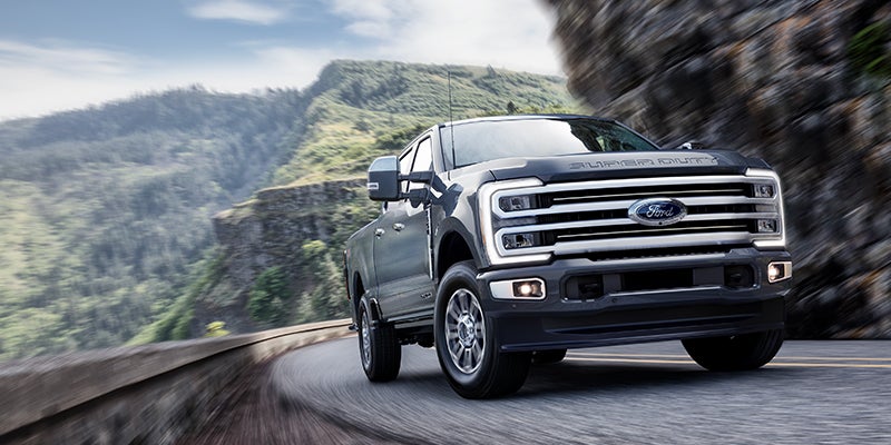 Dark gray Ford F-Series Super Duty truck driving on a winding cliffside road.