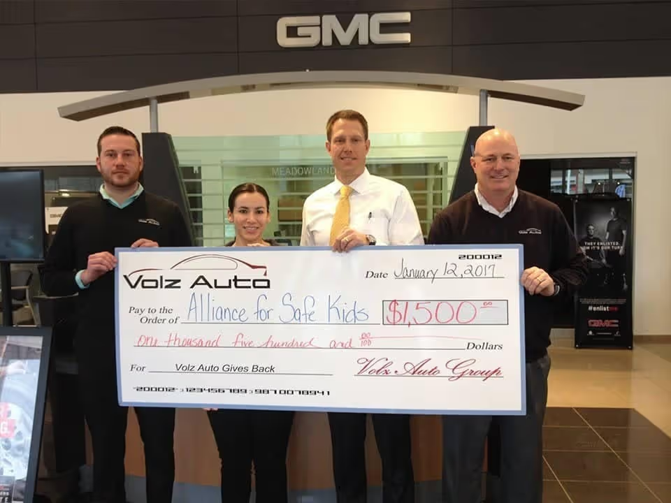 Group holding a large donation check inside a GMC dealership.