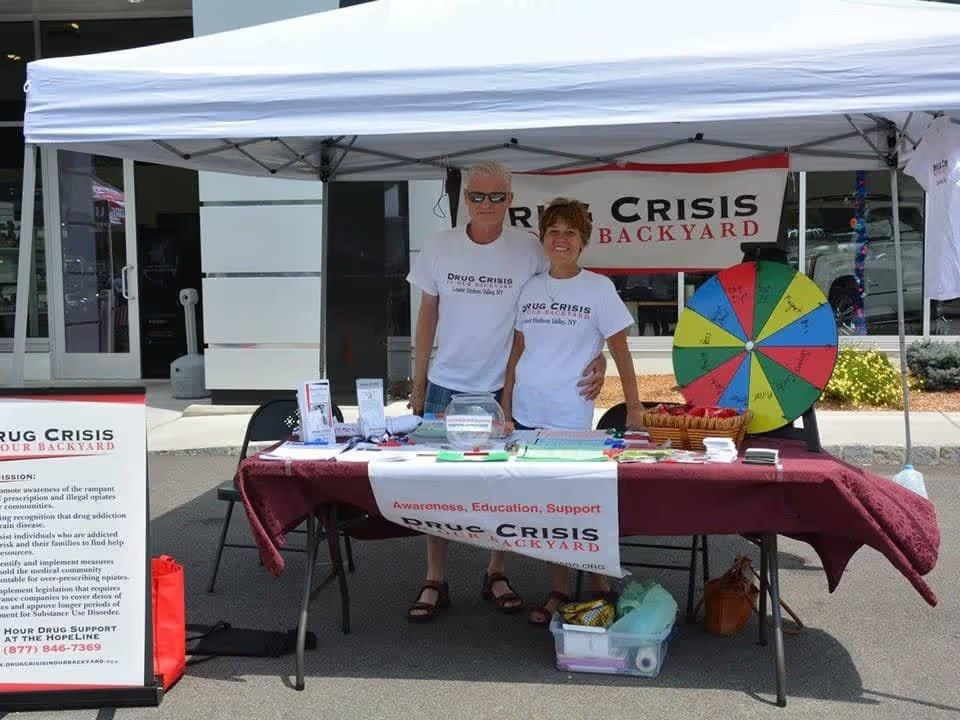 Two people at a Drug Crisis support booth under a tent.