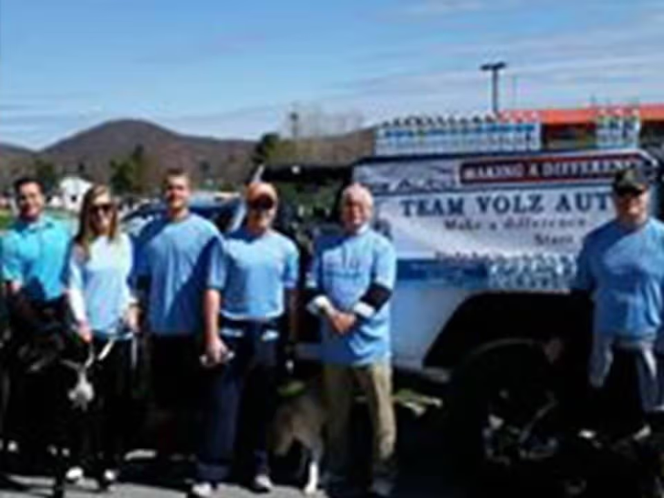 Group in blue shirts standing with a Team Volz Auto truck.