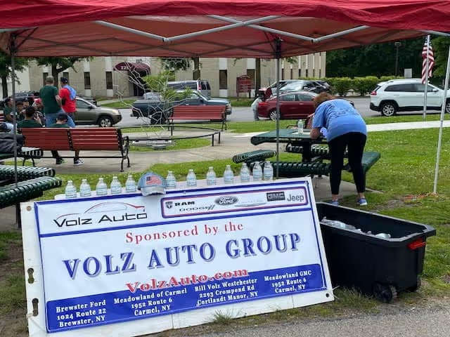 Volz Auto Group sponsor station with water bottles under a red tent.