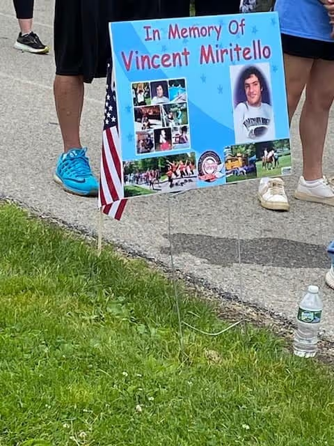 Memorial sign for Vincent Miritello with photos and an American flag.