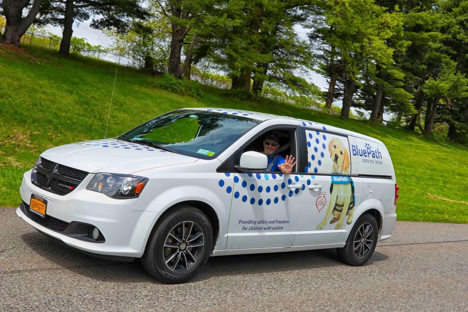 White 'BluePath Service Dogs' van with a man waving from window